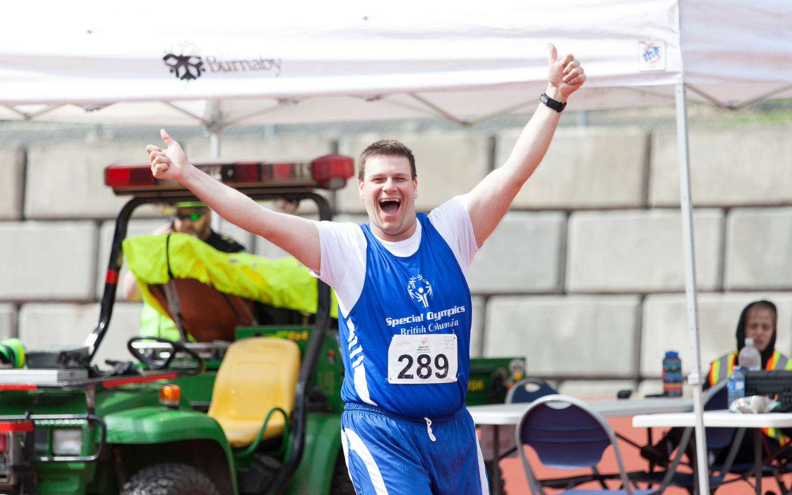 Special Olympics BC athlete gives an energetic two-thumbs up to the camera at a track and field meet.