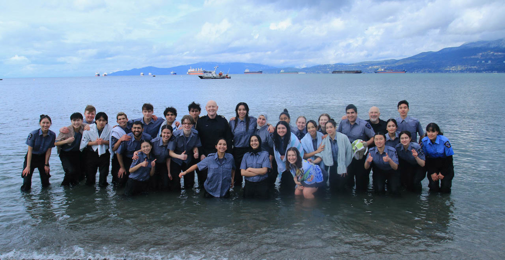 A large group of participants pose together in the shallow waters of English Bay looking proud.